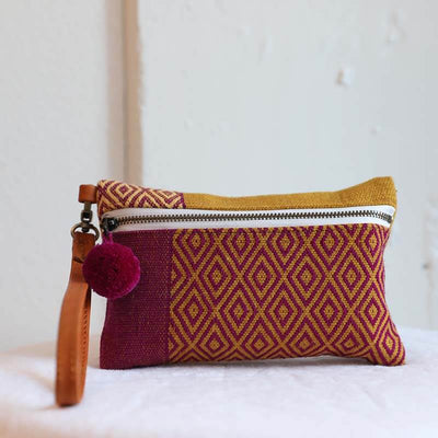 Magenta and yellow handwoven sheep wool wristlet with a tan leather strap features a nawi weave design and pom pom zipper detail