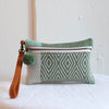 Olive handwoven sheep wool wristlet with a tan leather strap features a nawi weave design and pom pom zipper detail