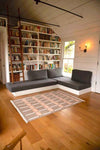 Ira Dhurrie Rug styled in living room placed on wood floor for a neutral accent surrounded by a bookshelf wall and grey couch