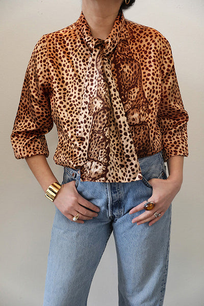 Featuring a stunning engineered placed leopard print with warm tones, this blouse boasts a unique jabot collar that adds a touch of elegance to any outfit.