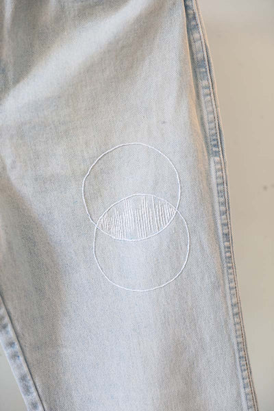 2 white circles overlapping each other in white on vintage wrangler denim handembroidered for Cura Collection