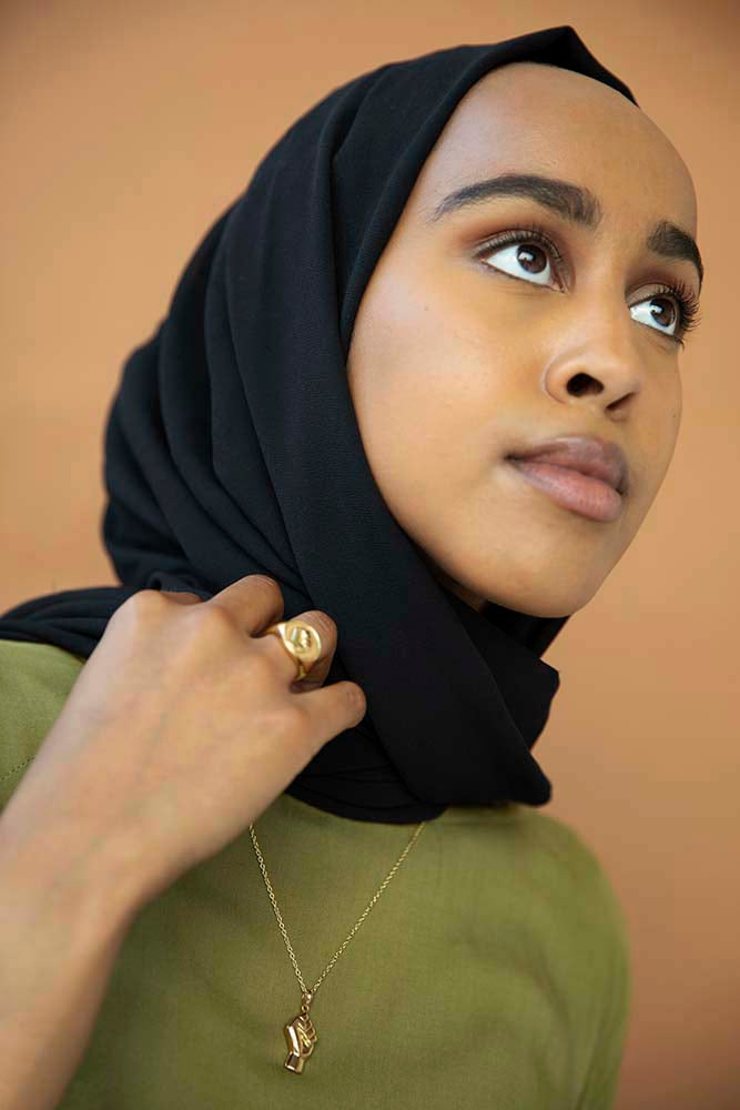Singer songwriter Hanan wears the This Matters BLM Power Pendant in sustainable brass. Ethically made in USA and Thailand. Designed by Akiko Waters founder of Cura and co-created with asian owned jewelry brand Boma.