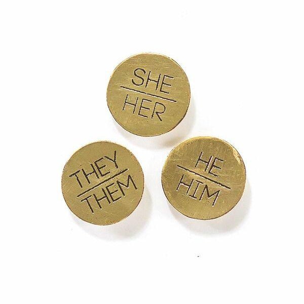 Pronoun pins made from upcycled brass saying she/her, they/them and he/him for Fair Anita