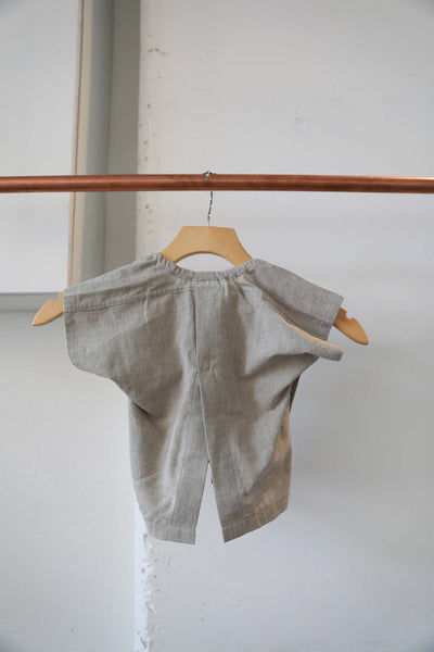 Back view of the grey blouse has an opening slit at the bottom and 2 button closures