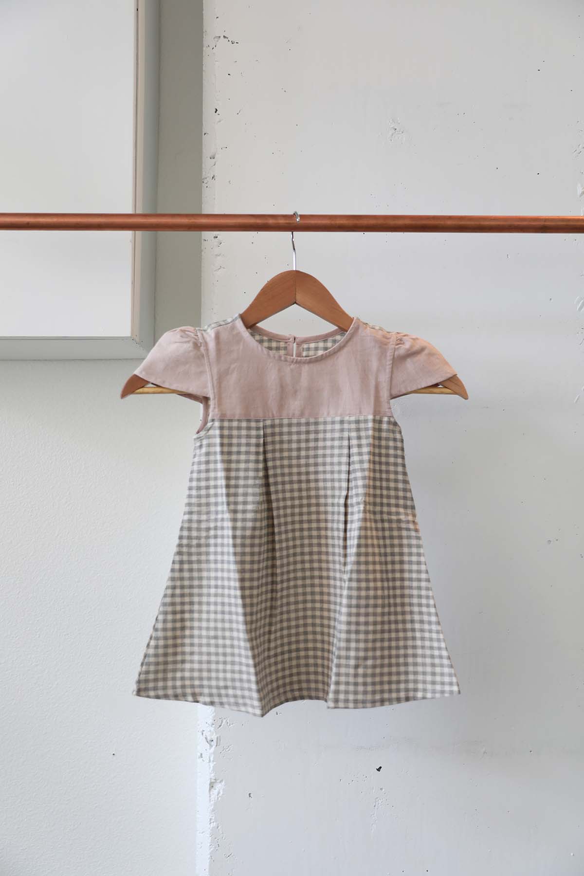 Girls dress with a pink top and plaid bottom in grey and cream with short sleeves ethically made by Goel Community in Cambodia