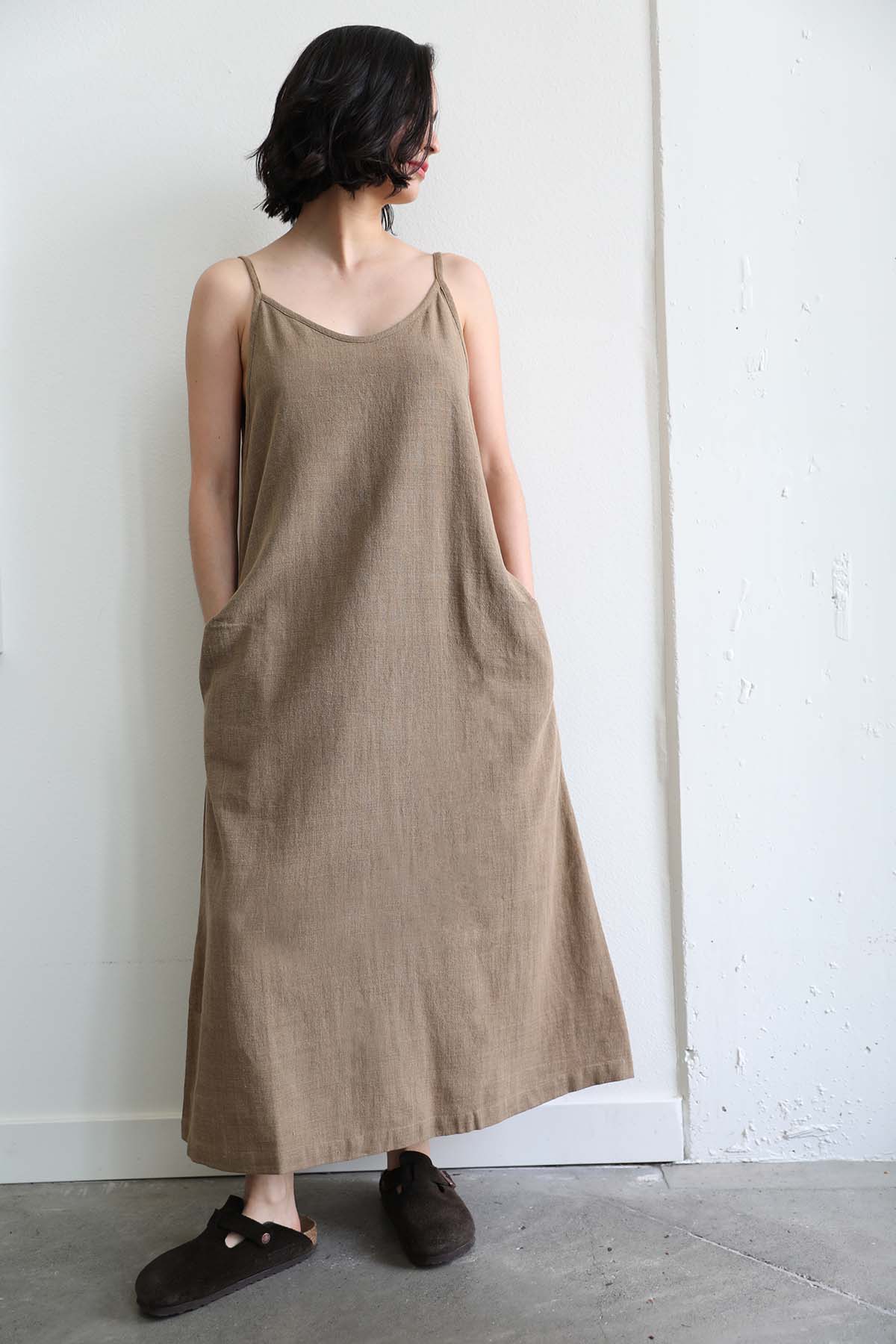 Brunette model with short hair wears the Brown Handloomed Dress showcasing the pockets paired with the Boston Suede Leather Birkenstock clogs in brown