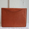 Back side of tan leather laptop case with a large pocket ideal for storing paper or a thin journal