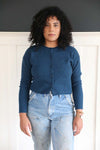 Curly haired model in a cropped blue cashmere cardigan by women-owned brand Joyride Supply