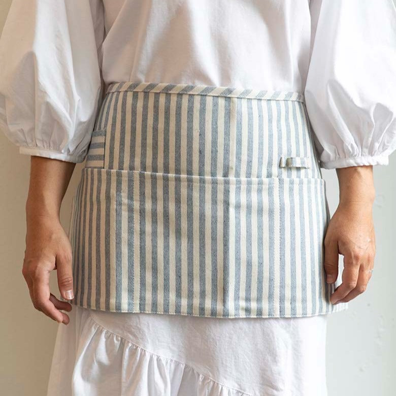 Women wears a sustainably made Striped Waist Apron by Meema. Designed with three large pockets, one small pocket and a utility loop to hang items from.