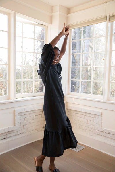 Moji wears the black Masako Midi dress with bracelet length sleeve, asymmetrical rushed hem detail part of the Hanae Collection by The Cura Co