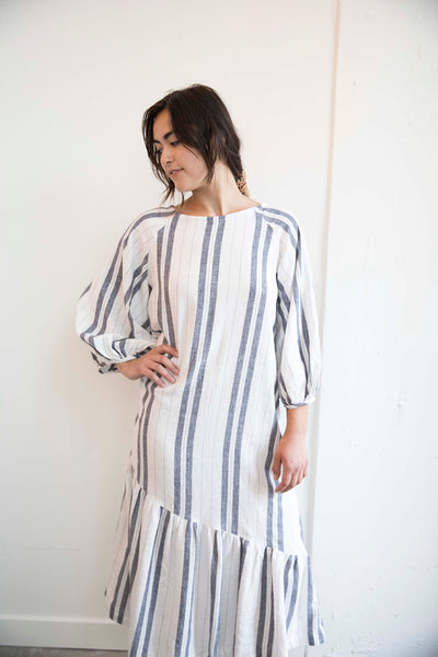 Sophia wears the pajama linen striped Masako Midi dress with bracelet length sleeve, asymmetrical rushed hem detail part of the Hanae Collection by The Cura Co