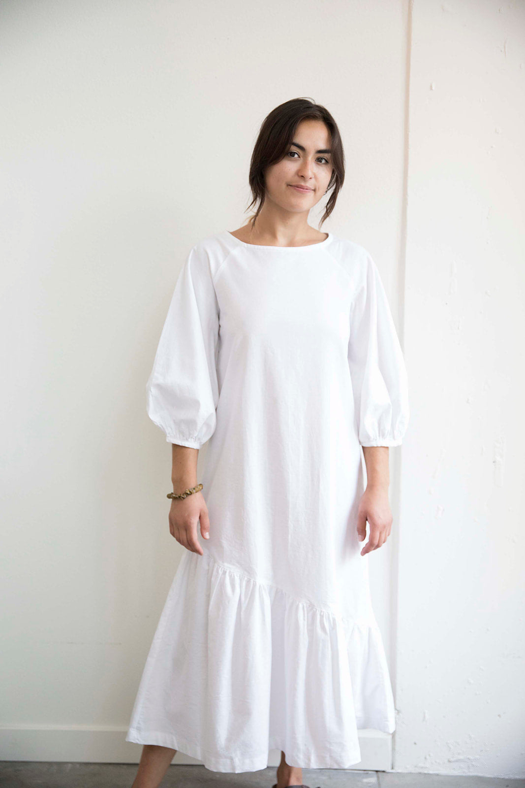 Sophia wears the white Masako Midi dress with bracelet length sleeve, asymmetrical rushed hem detail part of the Hanae Collection by The Cura Co