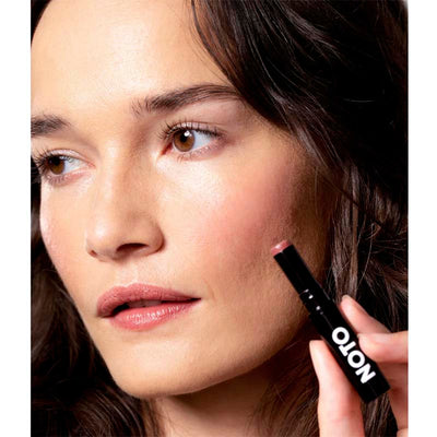 Fair skinned model wears the Five multi bene stick on her lips and cheeks while holding the beauty product. Appears as a light soft pink on her.