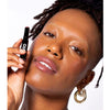 Dark skinned model wears the Five multi bene stick on her lips and cheeks while putting the lipstick while holding the product close to her cheek. Appears as a subtle soft taupe pink on her dewey skin.