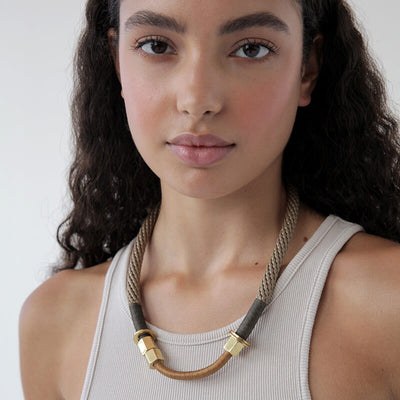 Curly haired brunette model wears a handmade rope necklace in beige orange and camel. Has two gold caps. Worn with a ribbed tank.