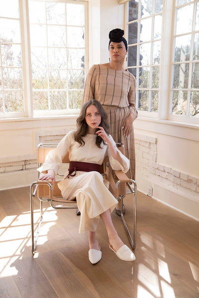 Kyla on chair wears the cream Tomoko Jumpsuit in Cream Herringbone and Taylor wears the Tomoko Dress part of the Hanae Collection by The Cura Co